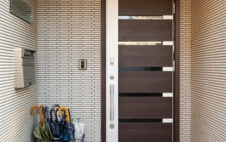 Contemporary entrance featuring a sleek wooden door with horizontal glass panels, set against a textured tiled wall. The area includes a black tiled floor and an umbrella stand with multiple umbrellas, adding a practical touch to the stylish design